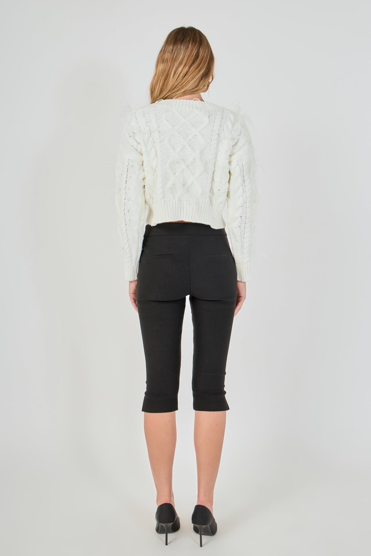 Straight-on rear view of cream cropped cable-knit sweater showing continuous back cable detailing and wide ribbed hem.