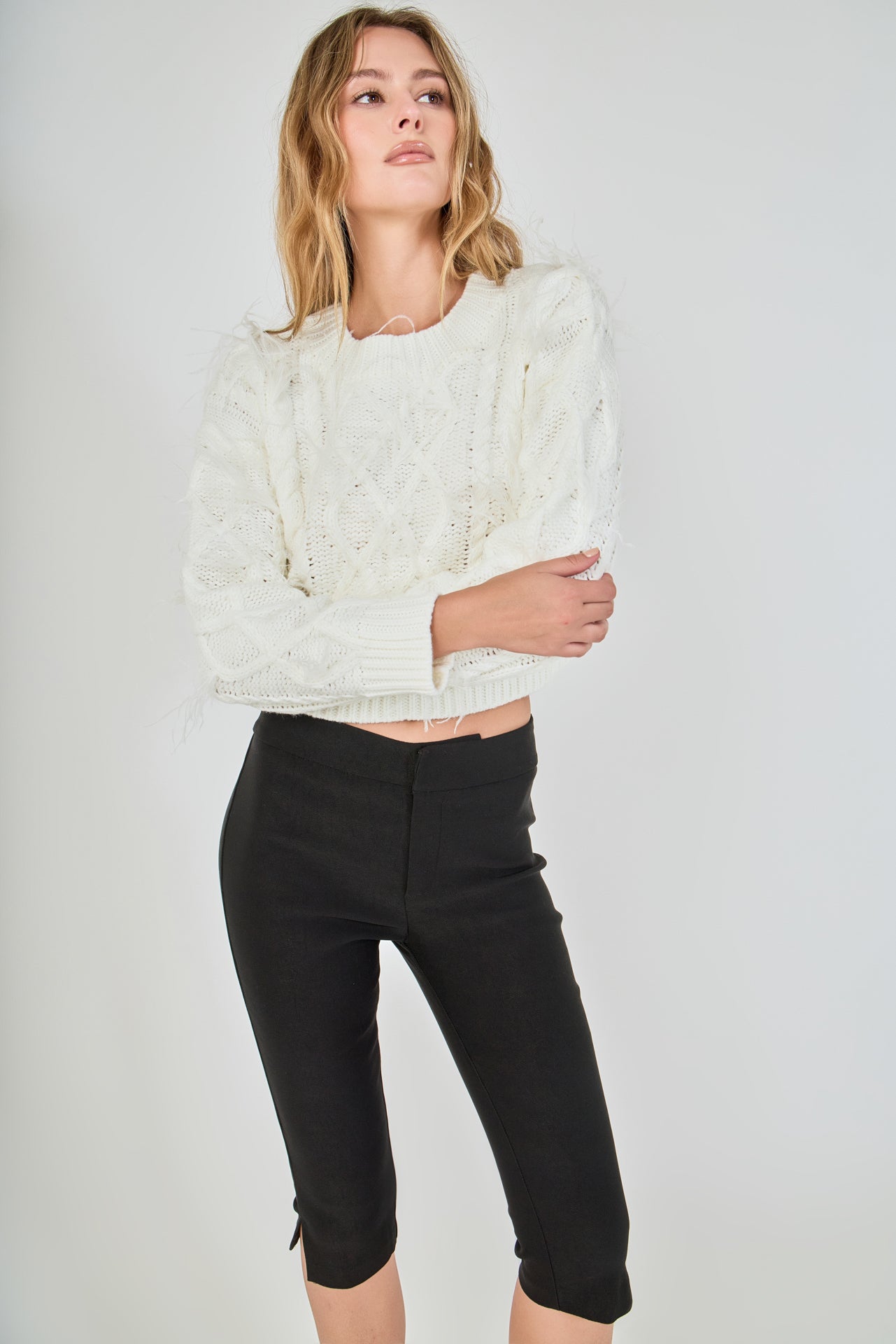 Face-forward posed view of a cream long-sleeve cable-knit cropped sweater featuring wispy feather accents woven throughout the cables.