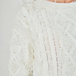 Ultra close-up detail view of cream cable-knit knitwear highlighting the diamond cable pattern and delicate wispy feather embellishments.