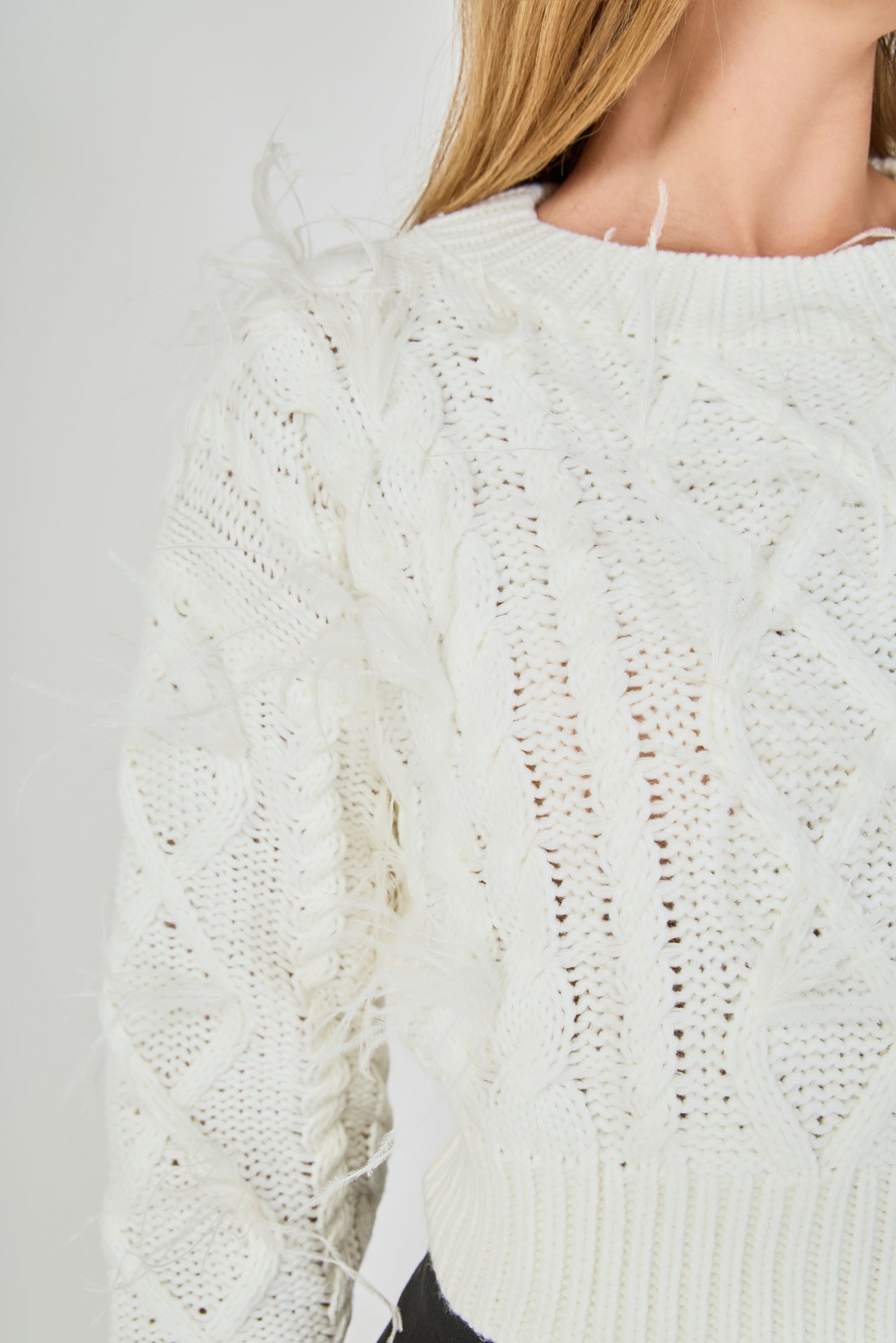Ultra close-up detail view of cream cable-knit knitwear highlighting the diamond cable pattern and delicate wispy feather embellishments.