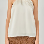 Upper body close-up view of an ivory satin halter top highlighting the draped crossover neck detail.