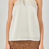 Upper body close-up view of an ivory satin halter top highlighting the draped crossover neck detail.