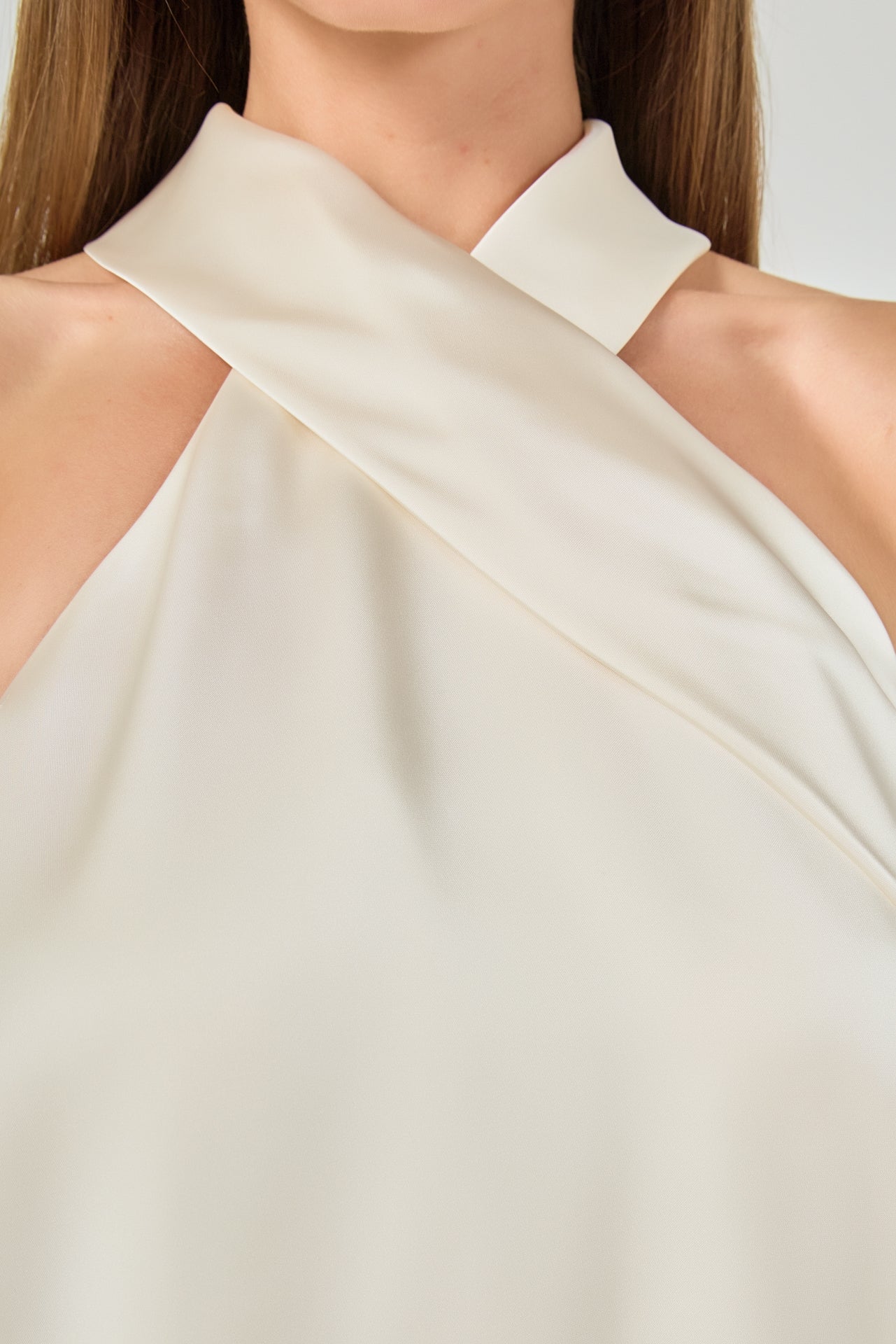 Ultra close-up detail view of smooth ivory satin fabric draped across the crossover halter neck.