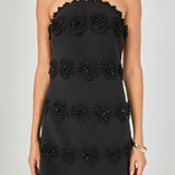 Close-up view of black strapless mini dress featuring a scalloped neckline and textured 3D floral appliqué trim.