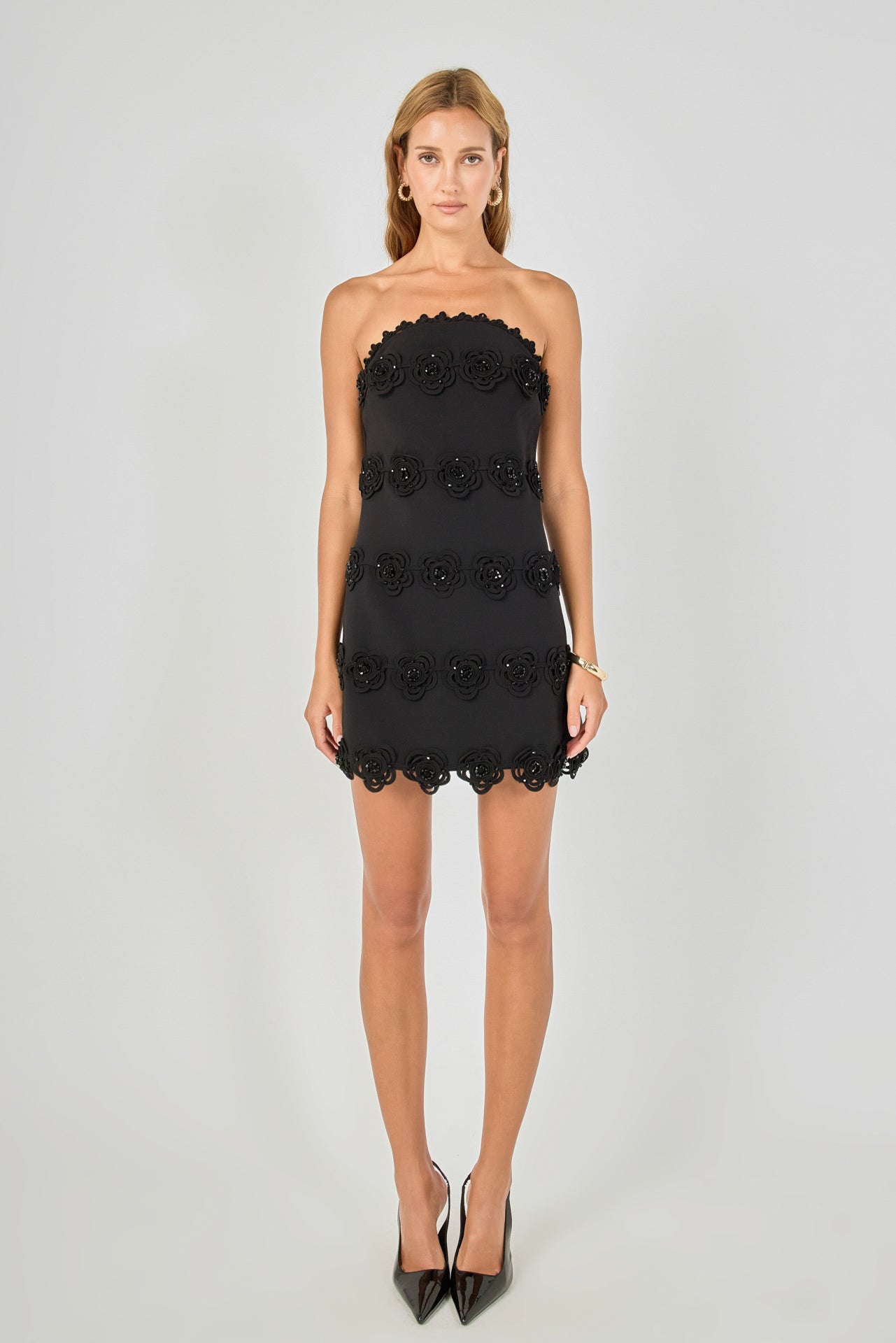 Black strapless mini dress featuring horizontal floral appliqué trim, scalloped neckline and hem, and a fitted silhouette.