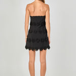 Back view of black strapless mini dress featuring horizontal floral appliqué trim and a straight hemline.