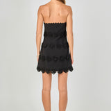 Back view of black strapless mini dress featuring horizontal floral appliqué trim and a straight hemline.