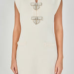 Upper body close-up view of a cream sleeveless knit mini dress showing the split neckline, cap shoulders, pearl bow embellishments, and faux hip pockets.