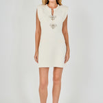 Full-length front view of a cream sleeveless knit mini dress featuring structured cap shoulders, double pearl bow placket detailing, and faux welt pockets.