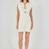 Full-length front view of a cream sleeveless knit mini dress featuring structured cap shoulders, double pearl bow placket detailing, and faux welt pockets.