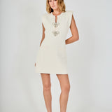 Face-forward posed view of a cream sleeveless knit mini dress with pearl bow accents, showcasing the complete look and silhouette.