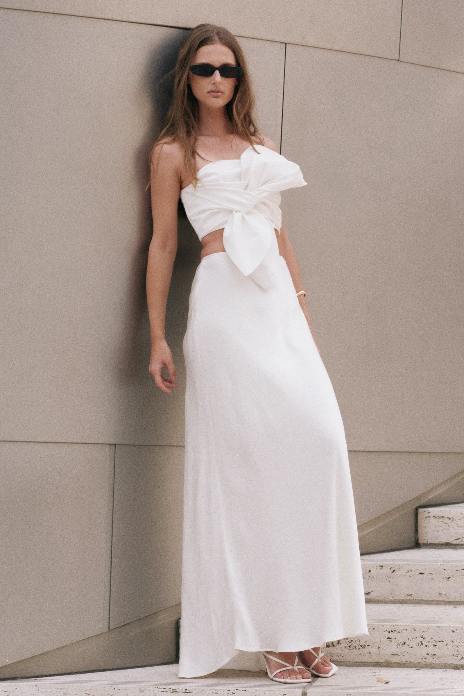 Three-quarter view of an ivory satin slip maxi skirt highlighting the high waistband and smooth, body-skimming fit.